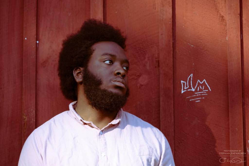 Tyler Donkoh-Halm's headshot. He stands close to the camera, smiling gently and looking out and up to the side.