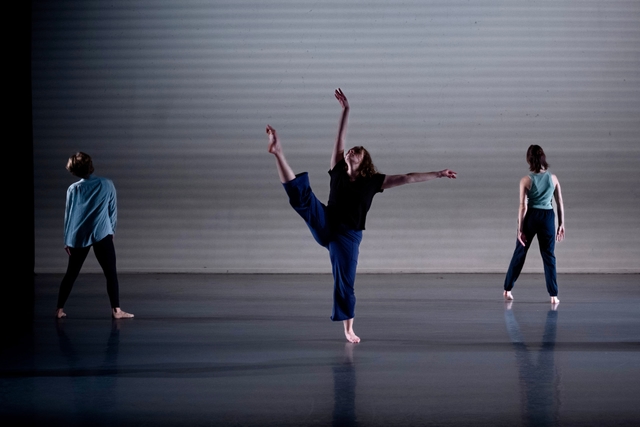 Hannah performing a grande-développé with her right leg lifted to the side and arms in an L-shape, surrounded by other dancers facing away