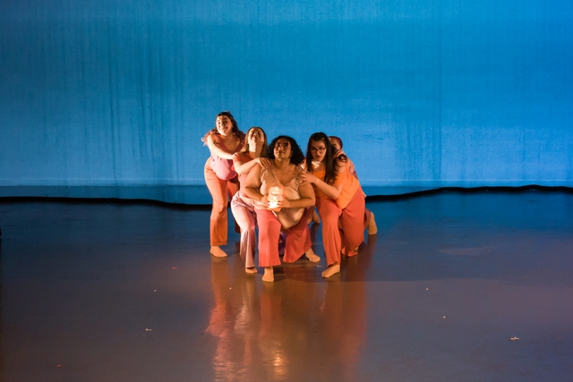 Five dancers in orange and pink costumes lunging forward while holding each other's shoulders, with the front dancer holding a lantern