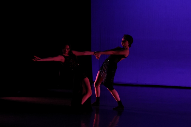 Two dancers in counter-balance holding each other's wrists, left dancer reaching toward audience while right dancer looks at their partner