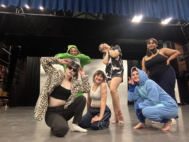 six people pose for the photo in two lines of three, wearing various halloween costumes and smiling at the camera.