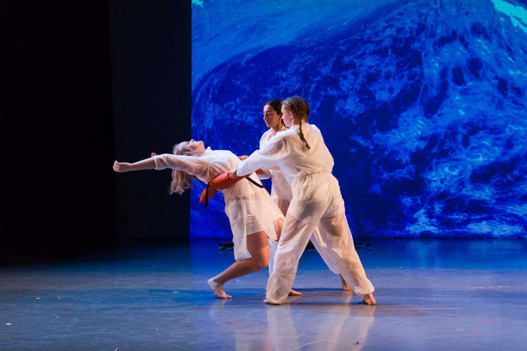 Hannah (front right) holds a life vest with another dancer, while a third dancer arches her back while leaning against the life jacket and extending her arms above her head.