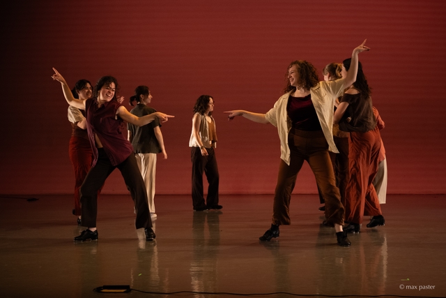Hannah and another dancer smile at each other with their arms extended in "disco" poses in opposite directions. Their fingers point outwards with energy.