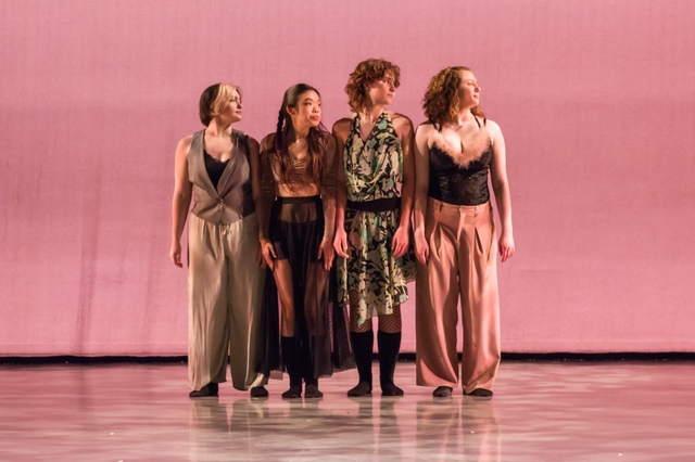 Four dancers stand close to each other, with their shoulders touching, facing the camera. They all have their heads turned to the right side of the screen.