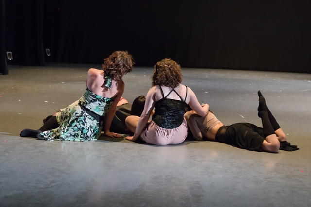 Four dancers sit on the floor, leaning against and lying on top of one another.