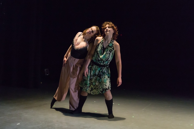 Two dancers stand next to each other, facing the camera. The one on the left (Hannah) leans against the one on the right. Both dancers close their eyes and smile peacefully.
